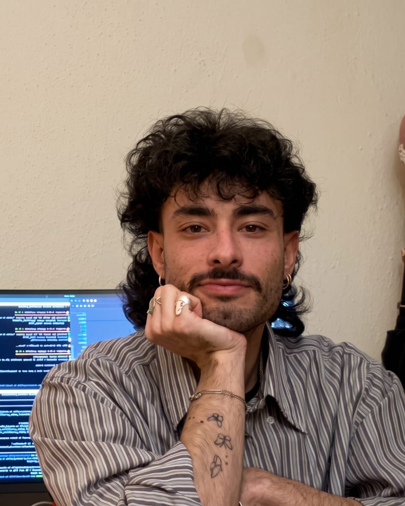 Luca Liverani at a desk, chin on his fist, a code editor on the screen behind him